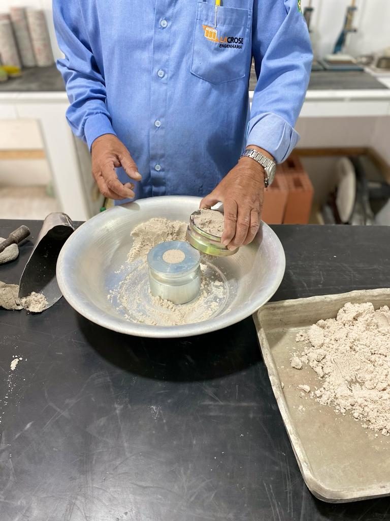 Técnico da LACROSE preparando amostra de solo em bacia de laboratório, preenchendo as cápsulas metálicas do ensaio.