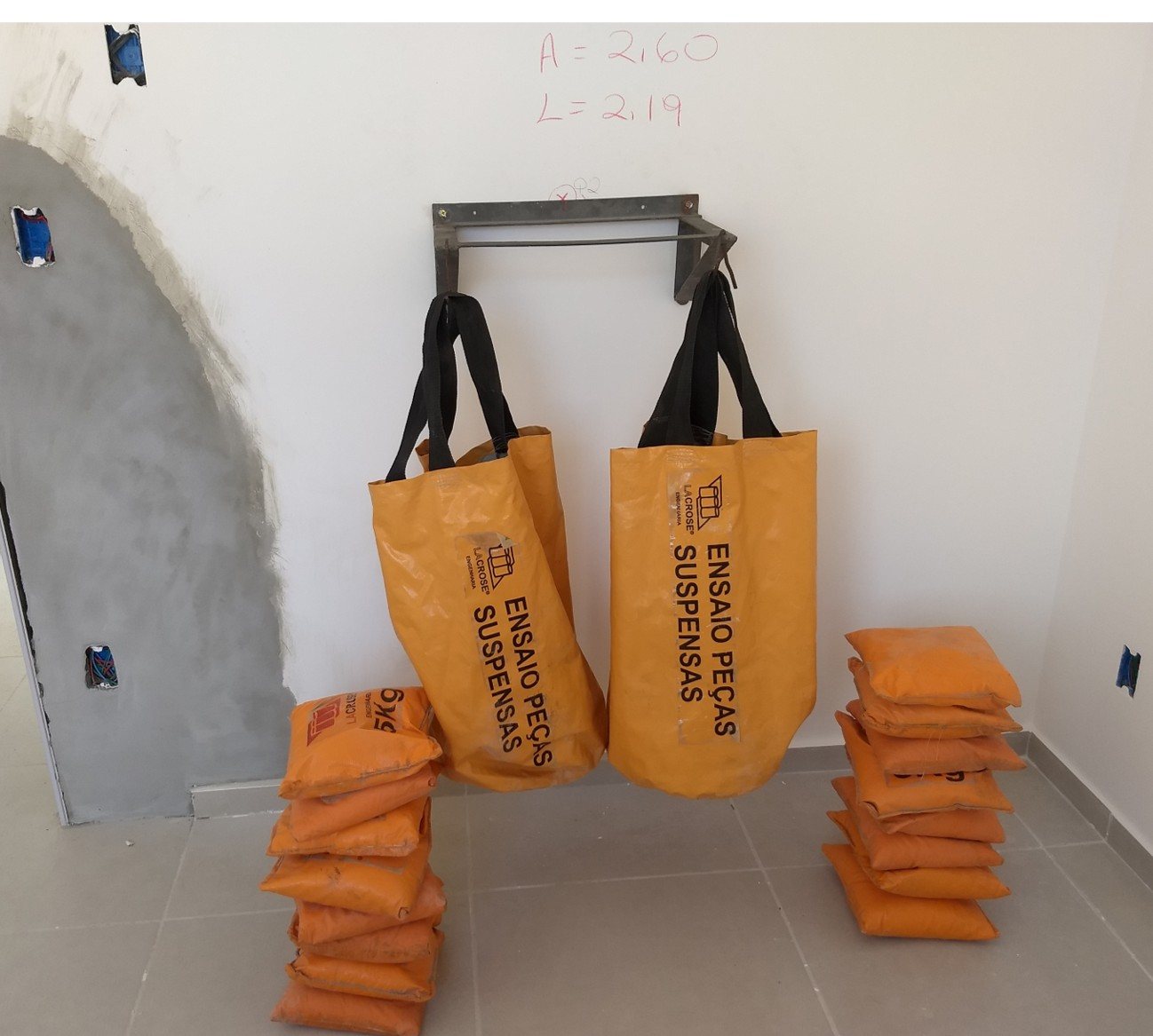 Sacos de carga da LACROSE pendurados em mão-francesa durante o ensaio de peças suspensas, com anilhas de lastro empilhadas ao lado.