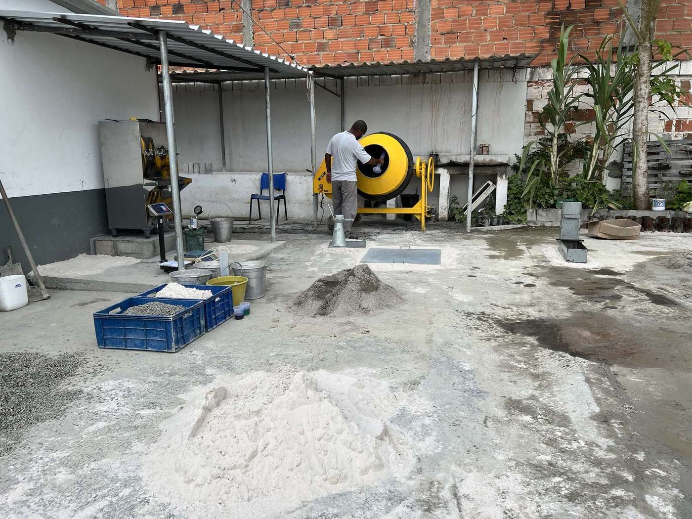 Técnico opera a betoneira durante estudo de dosagem de concreto em campo, com a bancada de ensaios ao lado.