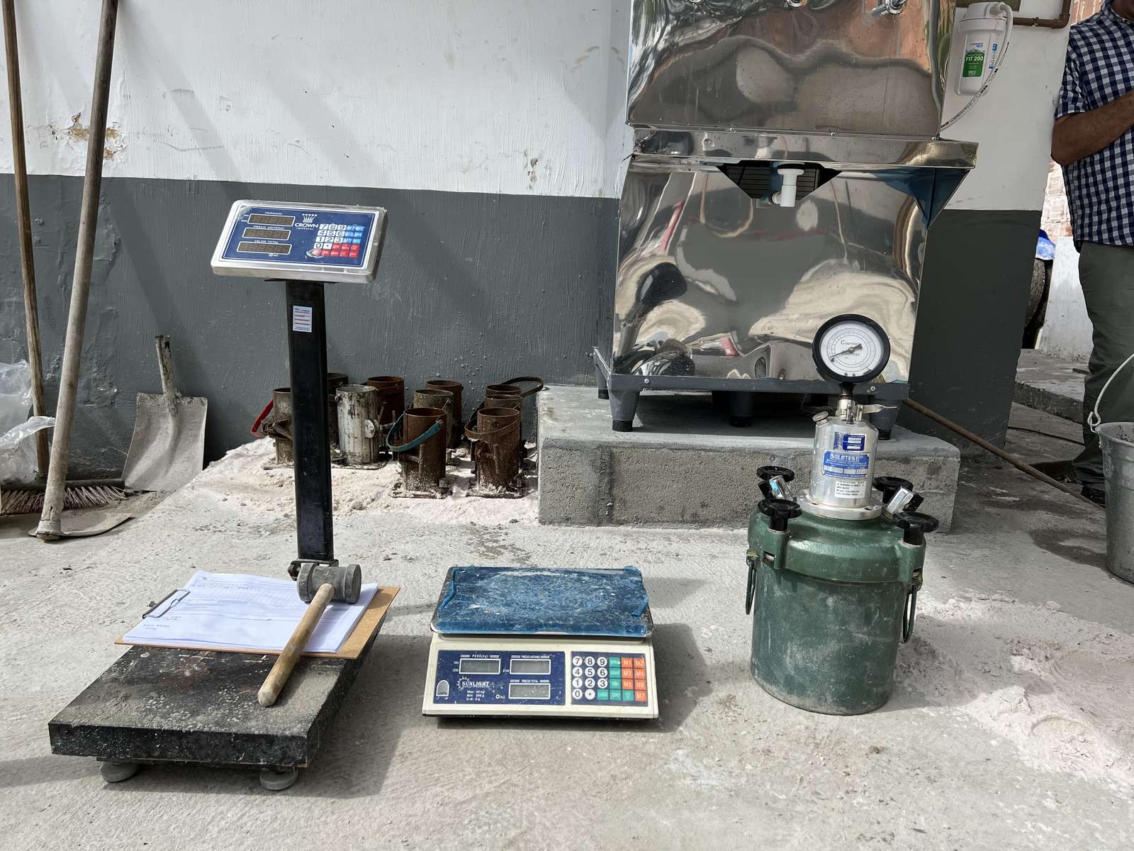 Balanças de plataforma e de precisão e medidor de ar incorporado preparados para o controle tecnológico do concreto, com moldes de corpos de prova ao fundo.