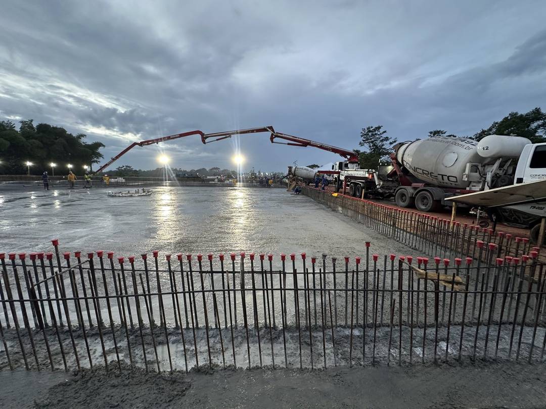 Concretagem noturna de laje: bomba lança em operação e equipe de obra uniformizada trabalhando sob iluminação artificial.