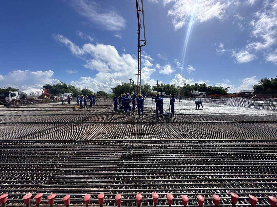 Equipe em campo sobre laje armada durante concretagem, com bomba lança em operação ao fundo.