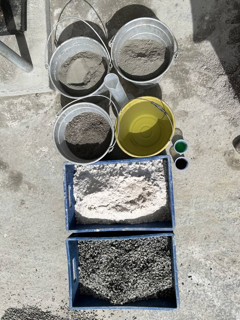 Materiais separados em bandejas e recipientes para dosagem de concreto em campo: cimento, areia, brita e aditivo.