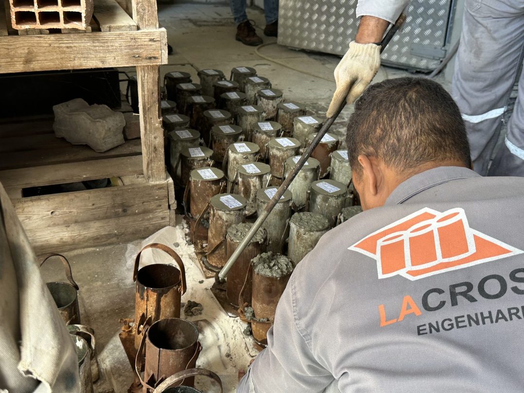 Técnico da LACROSE moldando corpos de prova cilíndricos de concreto em campo, com dezenas de moldes já preenchidos alinhados no canteiro.