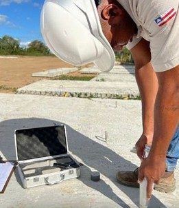 Técnico da LACROSE de capacete branco posicionando o esclerômetro sobre a laje de concreto durante o ensaio, com a maleta prateada do aparelho aberta ao lado.