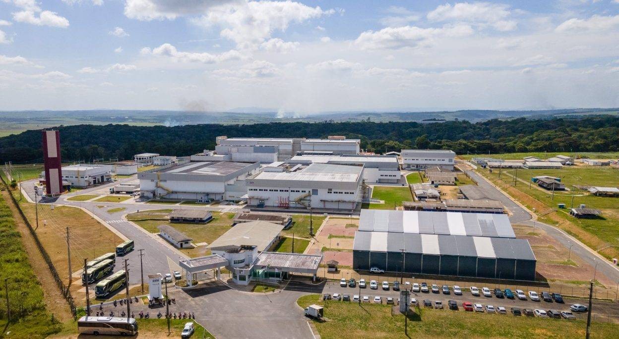 Vista aérea da unidade industrial da HEMOBRÁS em Goiana-PE, com os prédios fabris, a torre e o estacionamento em meio à área verde.